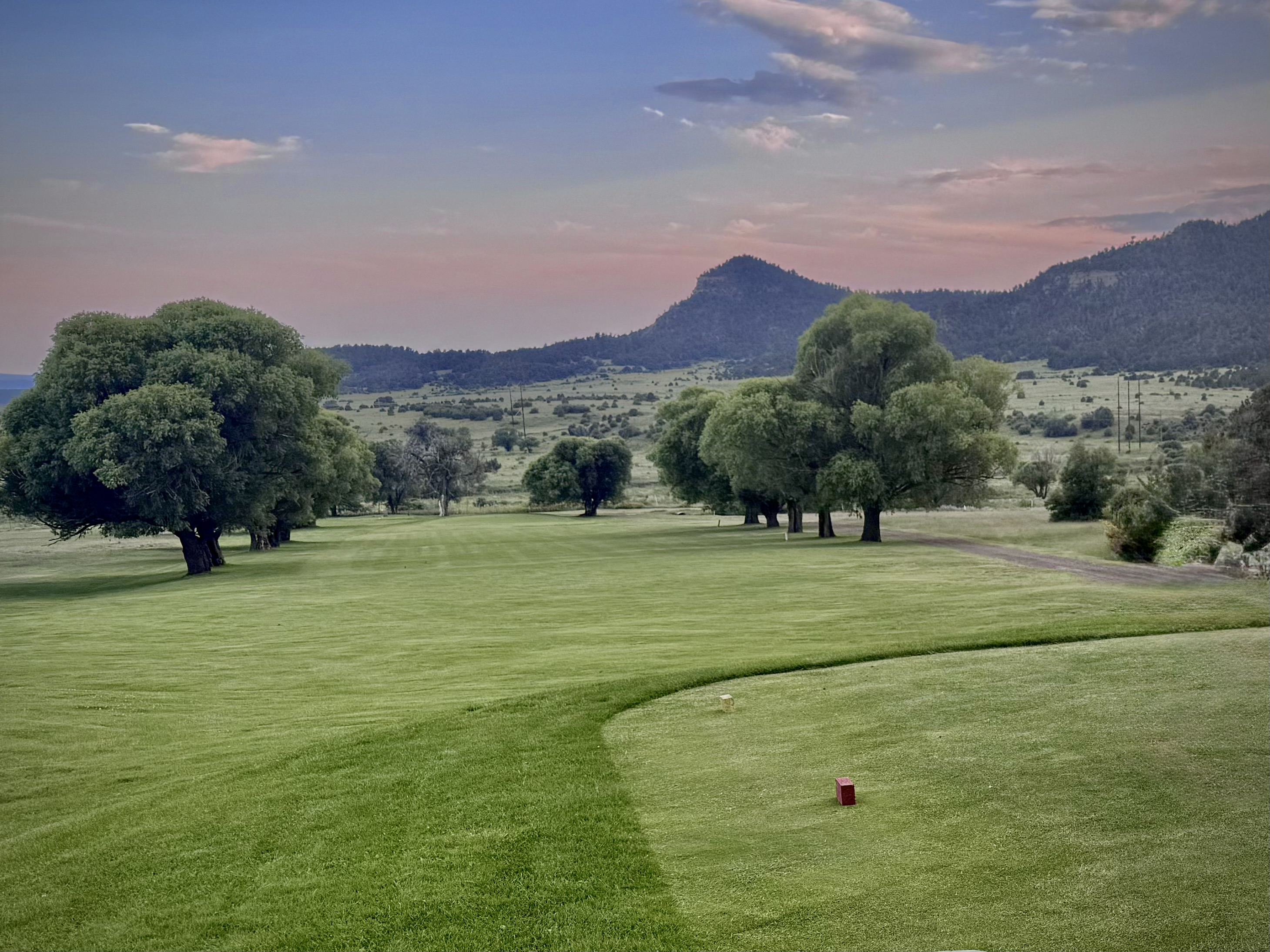 Manicured golf course greens at sunset with mountain range in distance